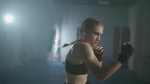 Junge Kämpferin trainiert seine Schläge im Boxstudio, Frau trainiert eine Reihe von Schlägen