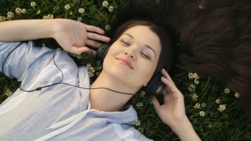 Frau hört Musik im Gras liegend