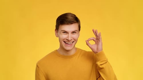 Smiling Man Gives Okay Sign on Yellow Background