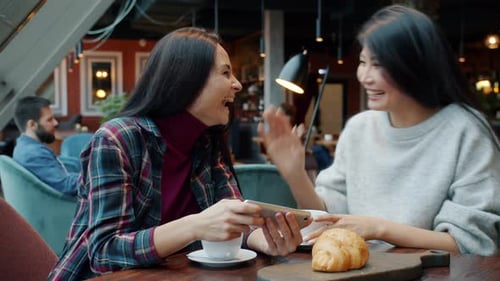 Women Friends Talking Laughing Looking at Smartphone Screen Then Doing High-five in Cafe