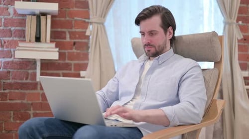 Man Working on Laptop in Chair at Home