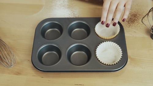 View of Female Hand Putting the Paper Cups Into the Baking Tray Woman Cooking Cupcakes.