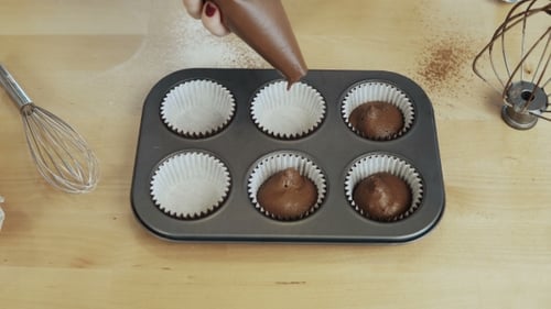 Vista de Manos femeninas poniendo la masa de la manga pastelera en los vasos de papel, en la bandeja para hornear