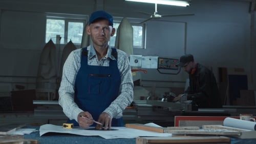 Man Marks Blueprint in Brightly Lit Workshop
