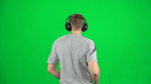 Man in Big Headphones Goes, Listening Music and Dancing on Green Screen at Studio. Back View. Slow