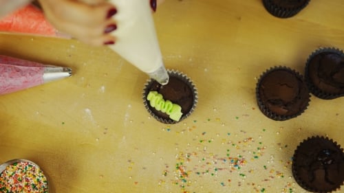 Hands decorating a chocolate cupcake with icing flowers