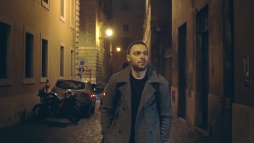 Young Handsome Man Walking Through the Deserted Street with Lights in the Evening Alone