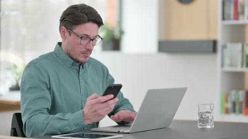 Man Uses Laptop and Phone in Home Office