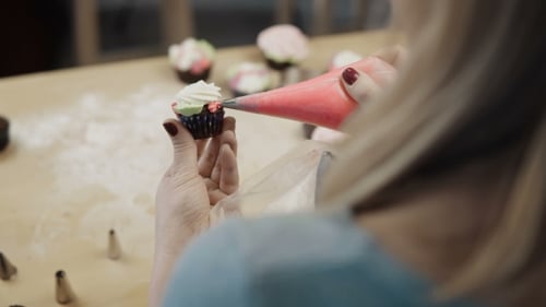Ansicht der weiblichen Hand, die den Schokoladen-Cupcake hält und ihn mit farbiger Creme dekoriert