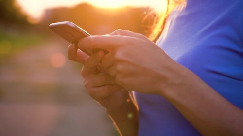 Woman Using Smartphone in Park at Sunset