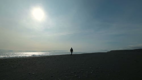 Young Man Walking on a Black Sandy Beach on a Mountain. During Vacation the Man Is in Warm Clothes