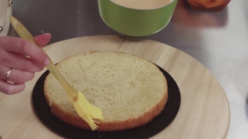 La pastelera femenina empapa el bizcocho con el líquido dulce