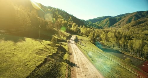 Low Air Flight Over Mountain Rural Dirt Road and Meadow at Sunny Summer Morning