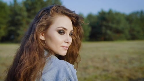 Young Stylish Smiling Girl with Long Hair and Beautiful Brown Eyes Having a Walk in the Field
