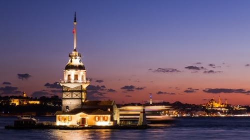 Maiden Tower oder Kiz Kulesi mit schwimmenden Touristenbooten auf dem Bosporus in Istanbul bei Nacht