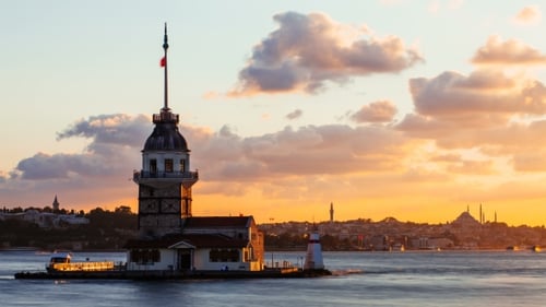 Maiden Tower oder Kiz Kulesi mit schwimmenden Touristenbooten auf dem Bosporus in Istanbul bei Sonnenuntergang