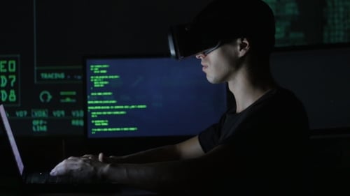 Young Man Using VR Headset Typing on Laptop