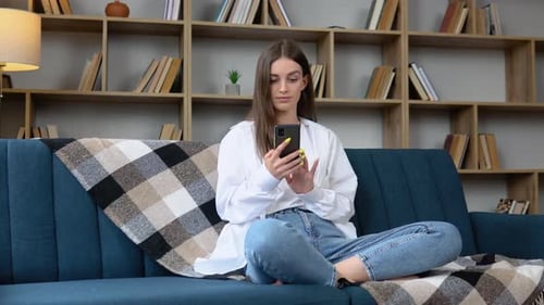 Young Woman Using Smartphone on Sofa at Home