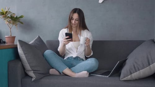 Woman Using Phone and Drinking Coffee on Couch