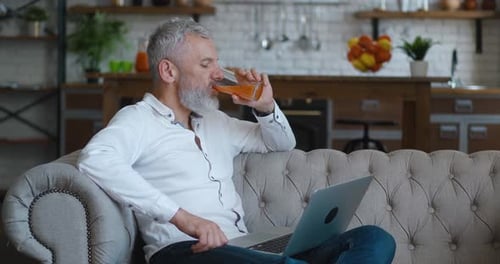Man Relaxing on Sofa with Laptop and Juice