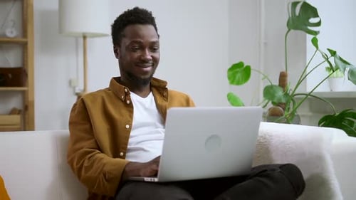 Young Adult Using Laptop on Sofa at Home
