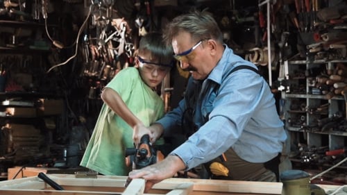 Child Learns Woodworking From Adult in Workshop