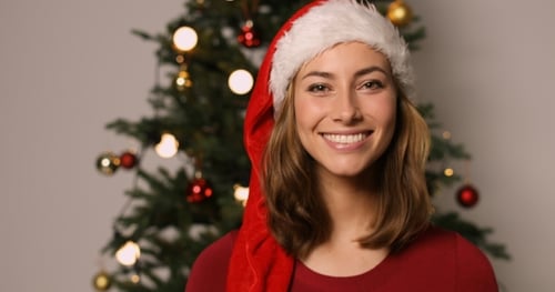 Smiling Woman Wearing a Santa Hat Near Christmas Tree