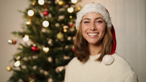 Happy Woman Wearing Santa Hat by Christmas Tree