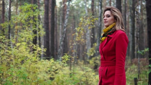 Young Woman in a Red Coat Walking Along an Autumn Park. Beautiful Girl Enjoying a Warm Autumn