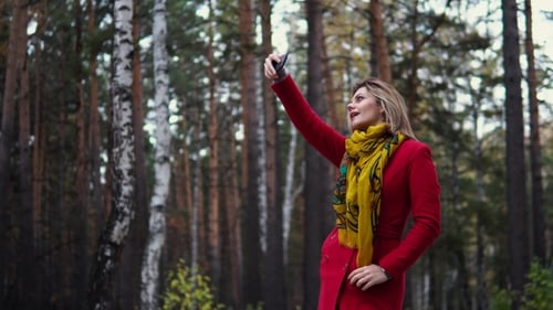 Young Woman in a Red Coat Walking Along an Autumn Park. Beautiful Girl Enjoying a Warm Autumn