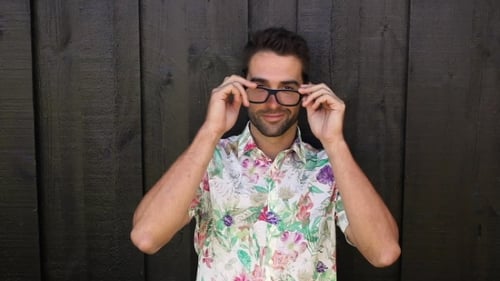 Young Man in Floral Shirt Puts On Glasses
