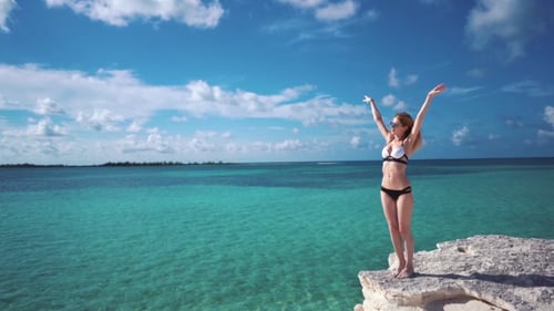 A Girl Stands on a Rock Against the Azure Water of the Caribbean Sea