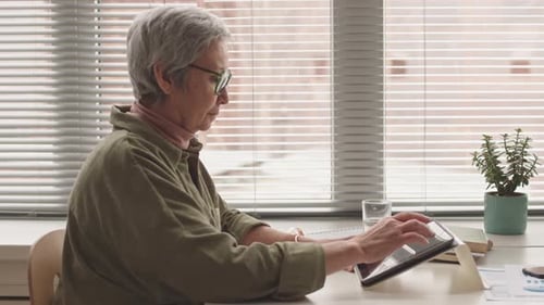 Senior Woman Using Tablet Device Indoors By Window