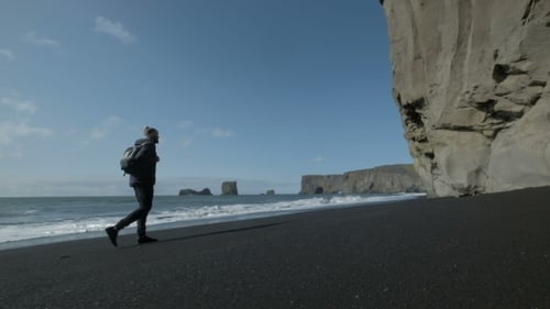 Man with a Backpack, Walking Along the Shore of Black Sand Beach in Iceland