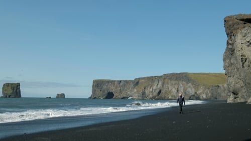 Man with a Backpack, Walking Along the Shore of Black Sand Beach in Iceland