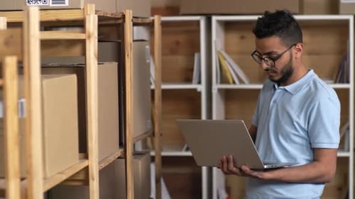 Asian Post Office Clerk with Laptop Performing Inventory of Parcels