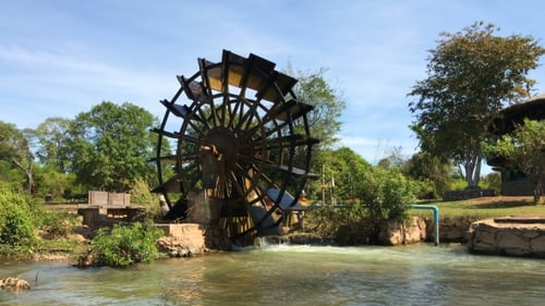 Funktionierendes Wassermühlen-Holzrad auf einem Fluss mit fallendem Wasser im Dorf