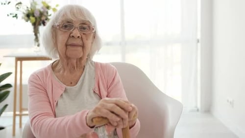 Senior Woman Sitting with Cane in Bright Room