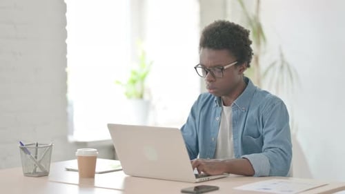 Young African Man Coughing While Using Laptop in Office