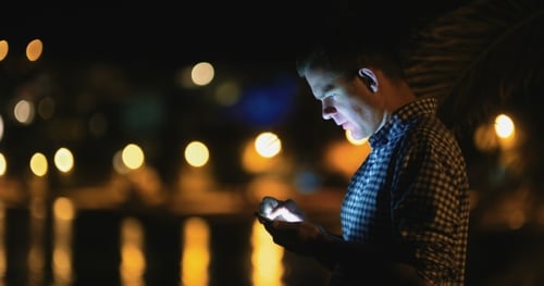 Man Using Smartphone at Night With City Lights