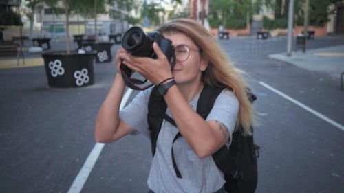 Woman Walking and Taking Pictures on Urban Street