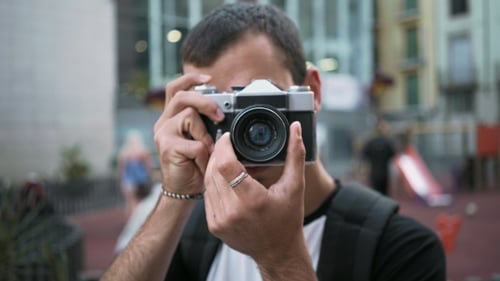 Young Man Walks with Camera in Old Town
