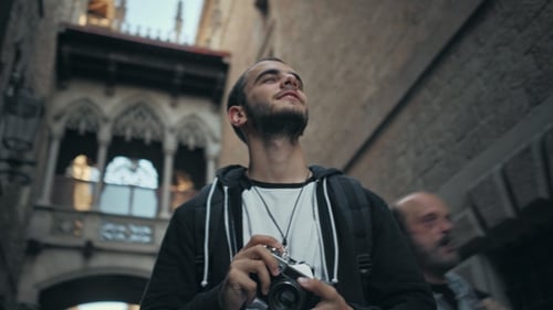 Young Man Walks with Camera in Old Town