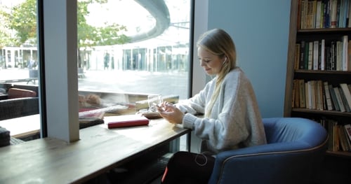 Young Woman Relaxing with Phone at Cafe Window
