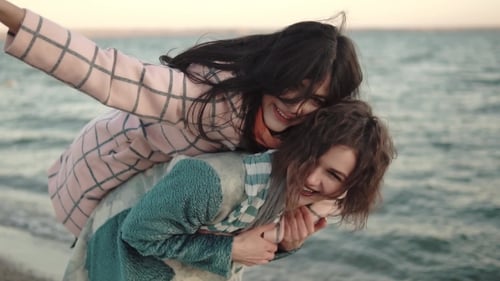 Two Women Piggyback Ride on Beach Having Fun