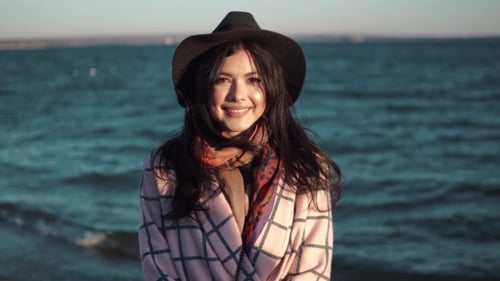 Portrait of a Young Woman on the Beach. Girl in Hat and Autumn Coat Smiling and Posing on Camera