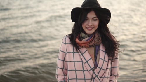 Portrait of a Young Woman on the Beach. Girl in Hat and Autumn Coat Smiling and Posing on Camera By