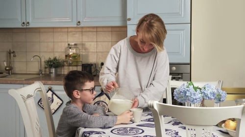 Woman Pours Milk for Child in Kitchen