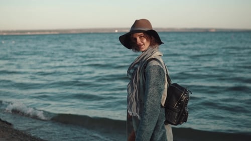 Beautiful Young Woman in Autumn Clothes Walks on the Beach at Sunset