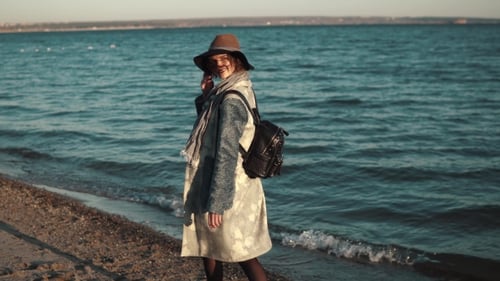 Beautiful Young Woman Walks Along the Coast, Smiling and Enjoying the Warm Autumn Day